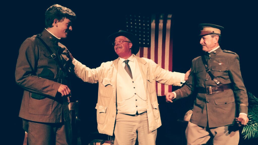 Joe as Roosevelt on stage with two other costumed performers